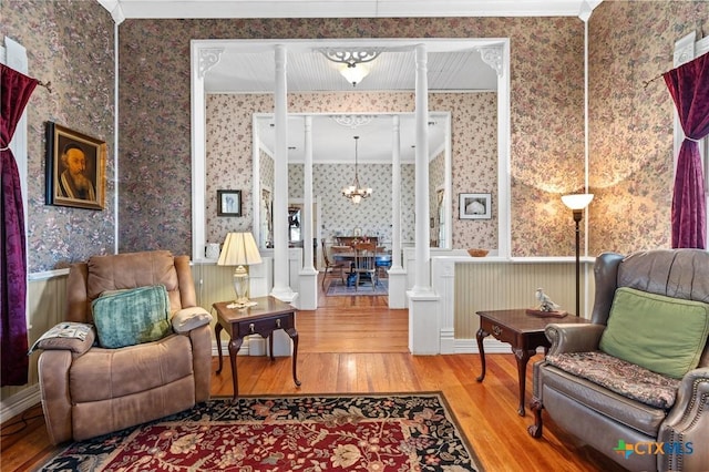 living room featuring wood-type flooring, decorative columns, an inviting chandelier, and crown molding