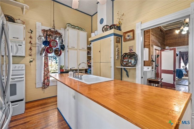 kitchen featuring stove, sink, hardwood / wood-style flooring, white cabinetry, and wood walls