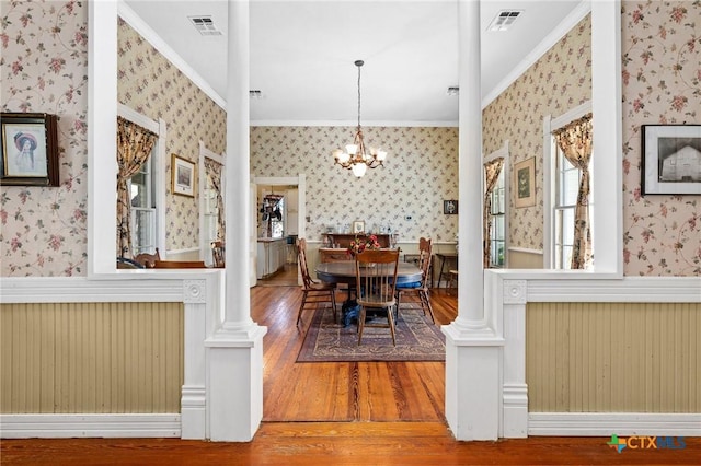 dining space with decorative columns, hardwood / wood-style floors, a notable chandelier, and ornamental molding