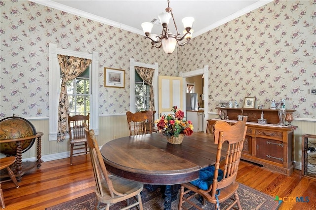 dining space with hardwood / wood-style flooring, ornamental molding, and an inviting chandelier