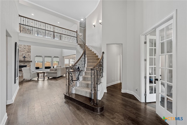 entrance foyer featuring a high ceiling, dark hardwood / wood-style flooring, a stone fireplace, and french doors