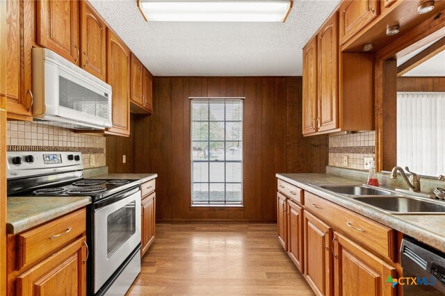 kitchen with stainless steel appliances, light hardwood / wood-style flooring, wooden walls, and sink