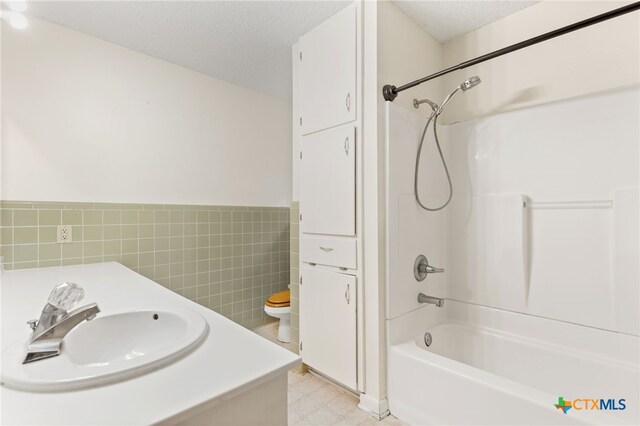 full bathroom with sink, a textured ceiling, toilet, shower / bathing tub combination, and tile walls