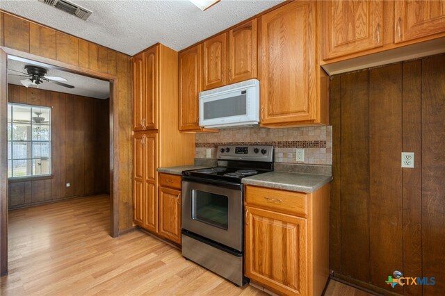 kitchen with stainless steel electric range, wood walls, light wood-type flooring, and ceiling fan