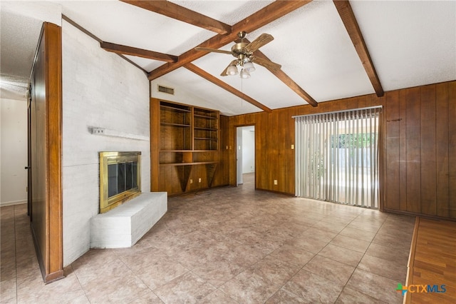 unfurnished living room featuring a fireplace, lofted ceiling with beams, ceiling fan, and wooden walls