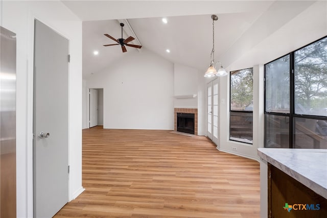 unfurnished living room with a fireplace, ceiling fan with notable chandelier, high vaulted ceiling, and light hardwood / wood-style flooring