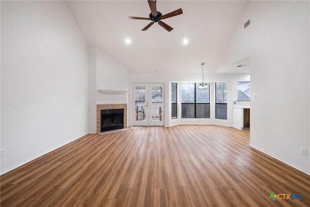 unfurnished living room featuring french doors, high vaulted ceiling, a fireplace, ceiling fan with notable chandelier, and light wood-type flooring