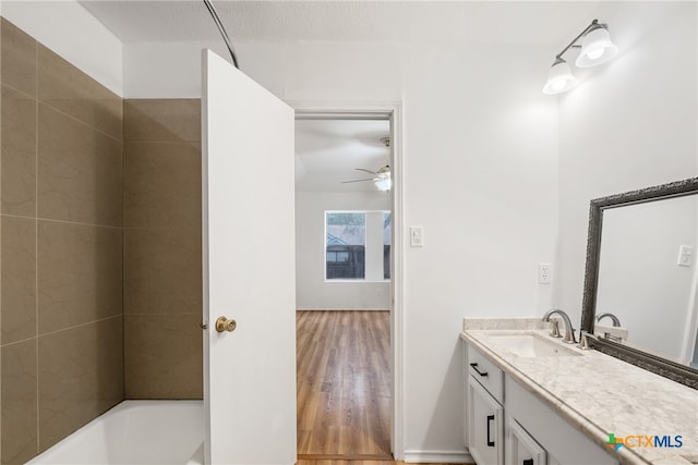 bathroom featuring vanity, hardwood / wood-style flooring, ceiling fan, tiled shower / bath combo, and a textured ceiling