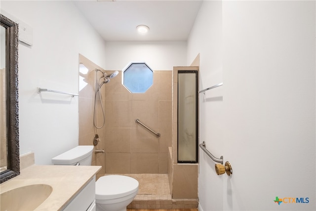 bathroom featuring tile patterned flooring, a tile shower, vanity, and toilet