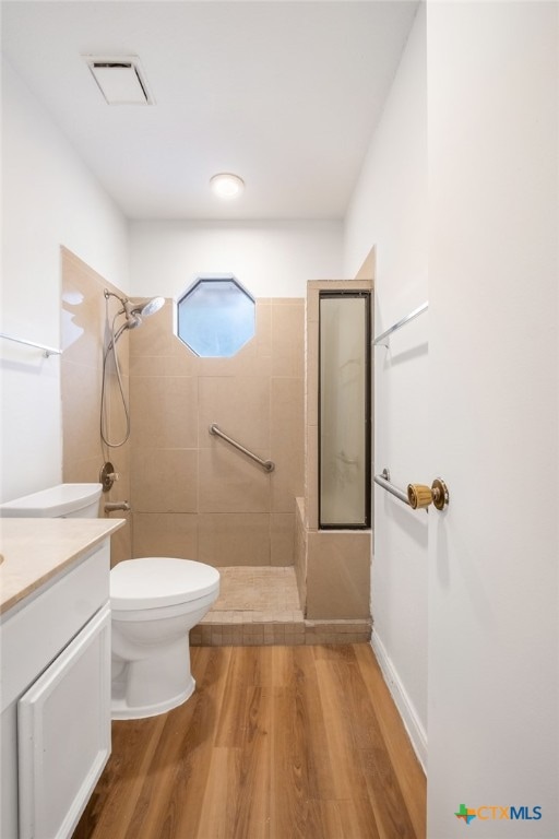 bathroom with tiled shower, wood-type flooring, vanity, and toilet