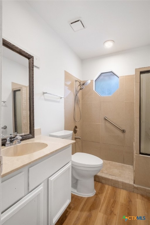 bathroom featuring tiled shower, vanity, wood-type flooring, and toilet