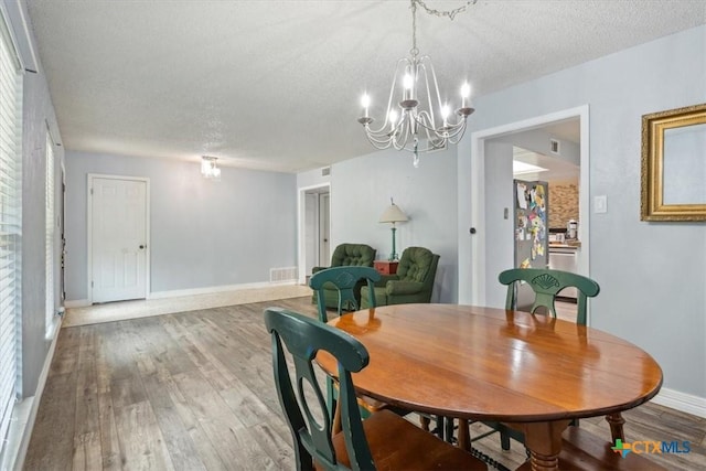 dining area with a chandelier, a textured ceiling, wood finished floors, and baseboards