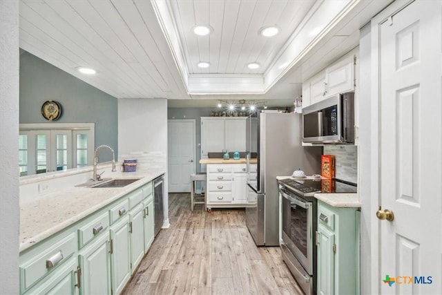 kitchen with stainless steel appliances, green cabinets, a sink, light wood-style floors, and a raised ceiling