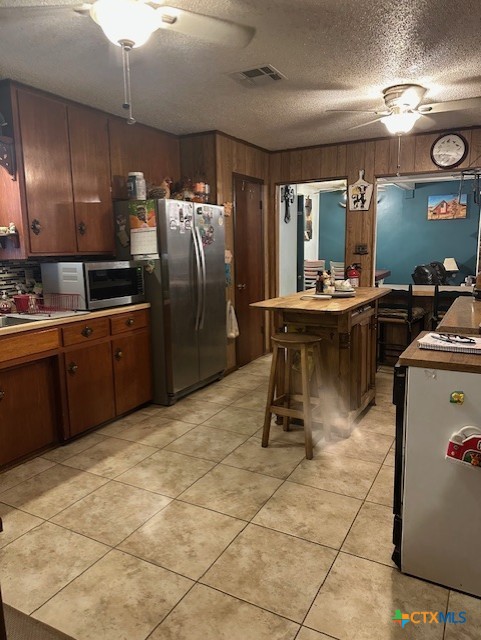 kitchen featuring wood walls, stainless steel appliances, visible vents, light tile patterned floors, and a textured ceiling