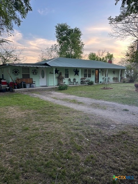 view of front of home featuring a lawn, a chimney, dirt driveway, covered porch, and metal roof