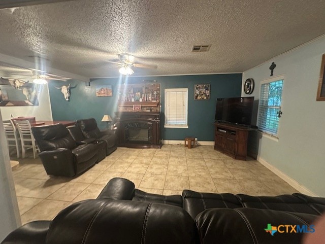 living area featuring visible vents, a ceiling fan, light tile patterned floors, baseboards, and a textured ceiling