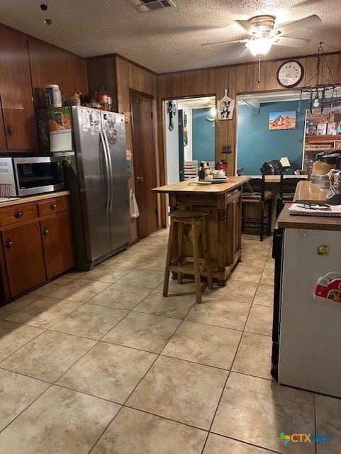 kitchen with wood walls, appliances with stainless steel finishes, a textured ceiling, and light tile patterned floors