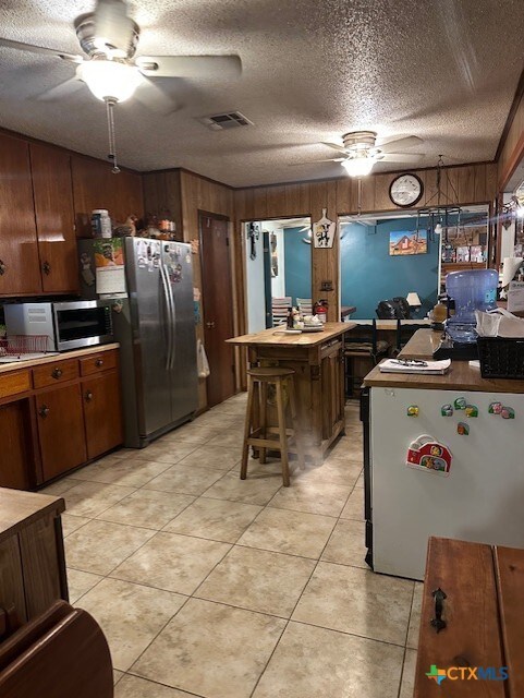 kitchen with ceiling fan, appliances with stainless steel finishes, wooden walls, and visible vents