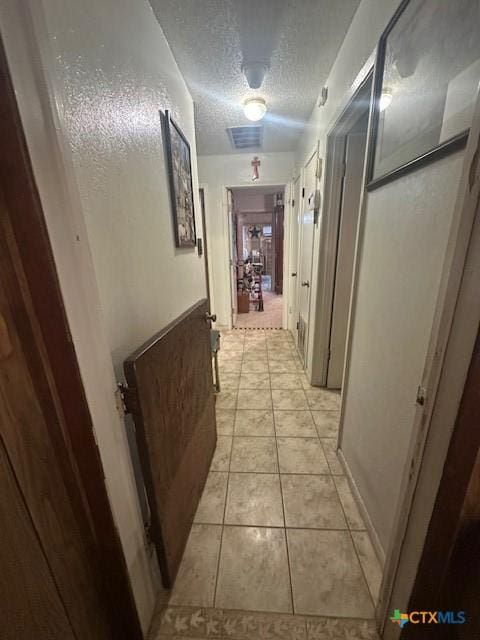 corridor featuring visible vents, a textured ceiling, and light tile patterned floors