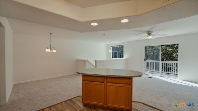 kitchen featuring ceiling fan with notable chandelier, light hardwood / wood-style floors, a kitchen island, and hanging light fixtures