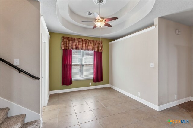 tiled spare room featuring a tray ceiling and ceiling fan