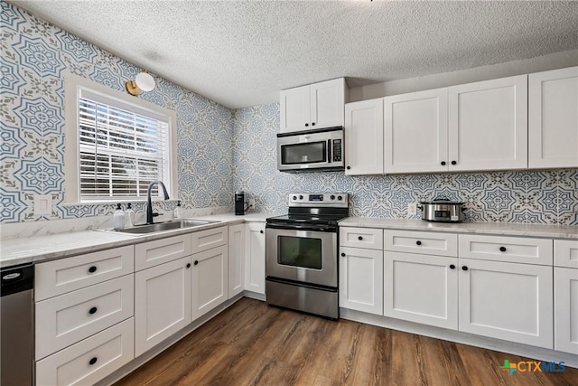 kitchen with dark wood-type flooring, sink, light stone countertops, white cabinetry, and stainless steel appliances