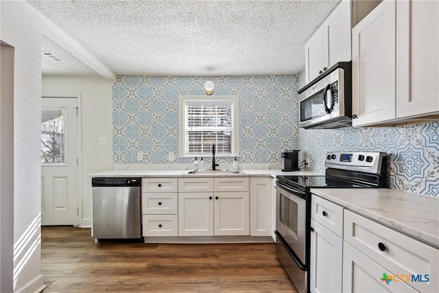 kitchen featuring white cabinetry, sink, stainless steel appliances, light stone counters, and dark hardwood / wood-style floors