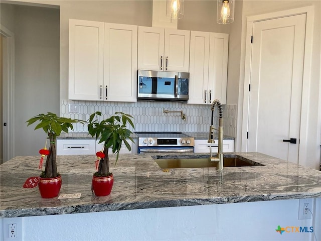 kitchen with dark stone countertops, sink, backsplash, stainless steel appliances, and white cabinets