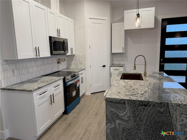 kitchen featuring hanging light fixtures, stainless steel appliances, light stone counters, sink, and white cabinetry