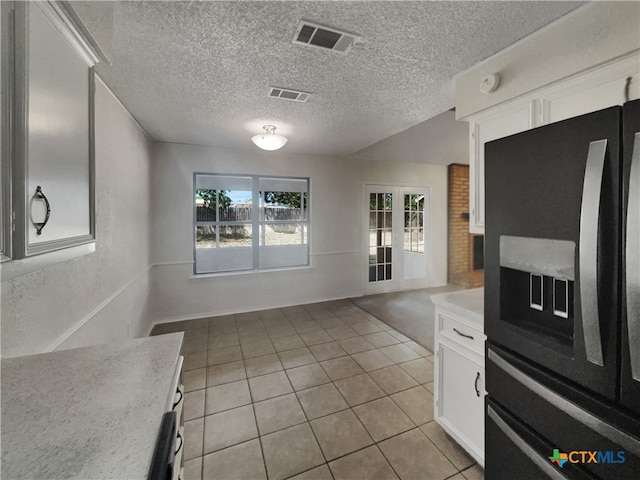 kitchen featuring light tile patterned flooring, white cabinetry, black fridge, a textured ceiling, and french doors