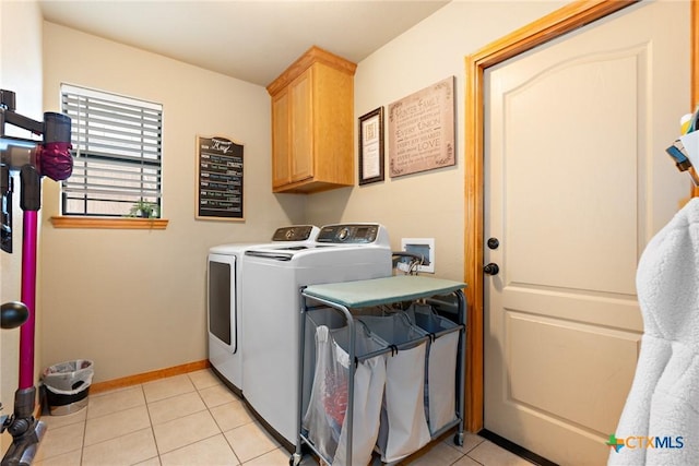 clothes washing area featuring washing machine and dryer, cabinet space, baseboards, and light tile patterned flooring