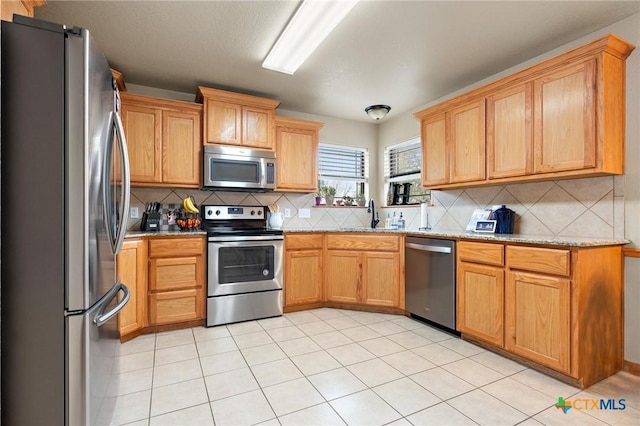 kitchen featuring a sink, appliances with stainless steel finishes, decorative backsplash, and light stone counters