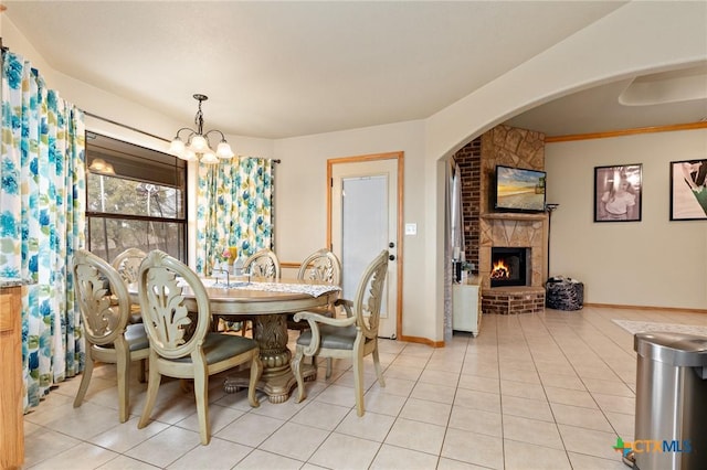 dining room featuring a chandelier, arched walkways, light tile patterned flooring, a fireplace, and baseboards