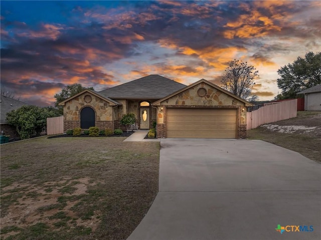 view of front of home with an attached garage, brick siding, fence, concrete driveway, and a lawn