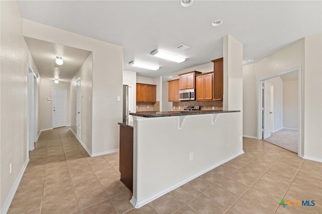 6208 Suellen Ln, Killeen, TX 76542 - kitchen featuring stainless steel microwave, light tile patterned flooring, backsplash, brown cabinetry, and a breakfast bar