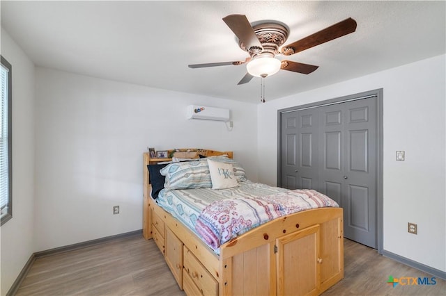 bedroom featuring baseboards, a closet, light wood-type flooring, and a wall mounted AC