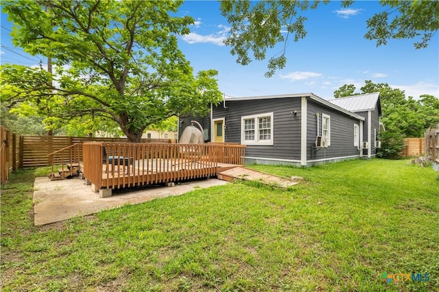 back of property with a fenced backyard, a wooden deck, metal roof, and a lawn
