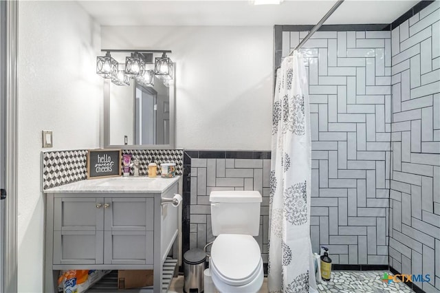 full bath with toilet, tiled shower, a wainscoted wall, tile walls, and vanity