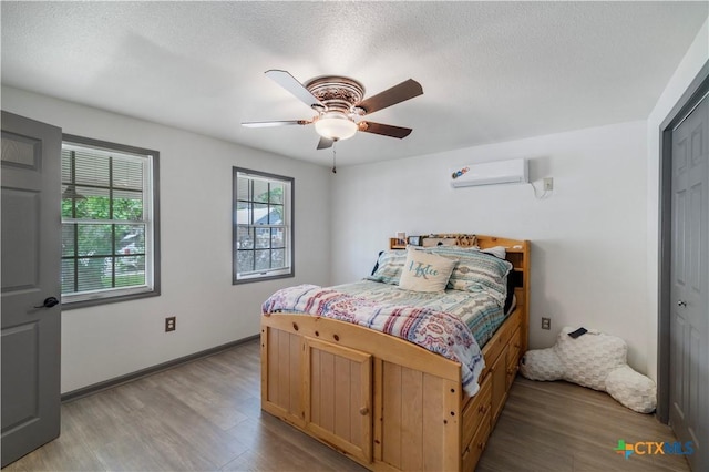 bedroom with ceiling fan, wood finished floors, baseboards, and a wall mounted AC