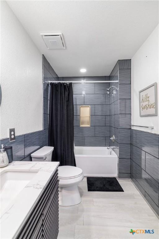 full bathroom featuring tile walls, toilet, shower / tub combo with curtain, visible vents, and vanity