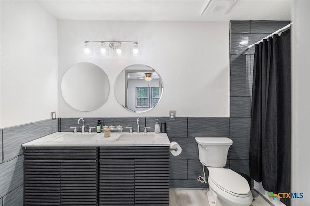 full bath with toilet, tile walls, double vanity, and a sink