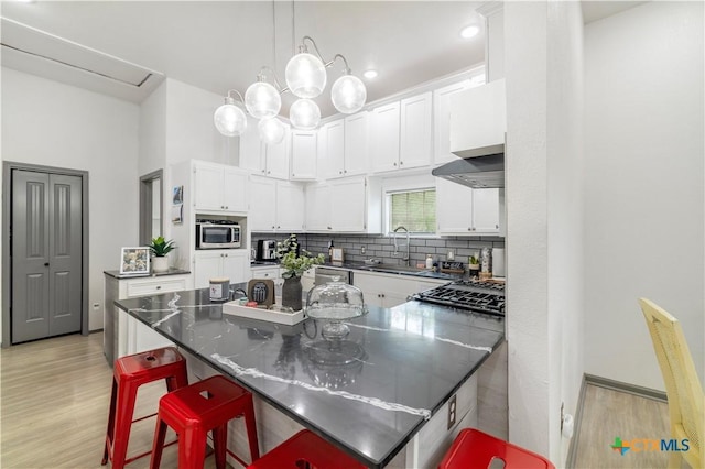 kitchen featuring a peninsula, a sink, white cabinetry, backsplash, and light wood-style floors