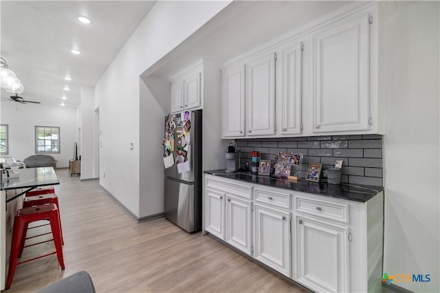kitchen featuring freestanding refrigerator, light wood-type flooring, backsplash, a ceiling fan, and white cabinets