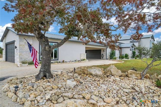 view of front of house featuring stucco siding, a standing seam roof, stone siding, an attached garage, and metal roof