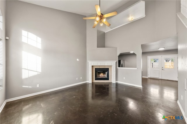 unfurnished living room with a tiled fireplace, ceiling fan, and a high ceiling