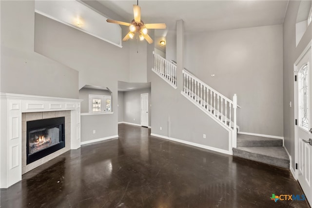 unfurnished living room with a tile fireplace, a high ceiling, and ceiling fan