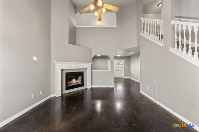 unfurnished living room with ceiling fan, a towering ceiling, and a fireplace