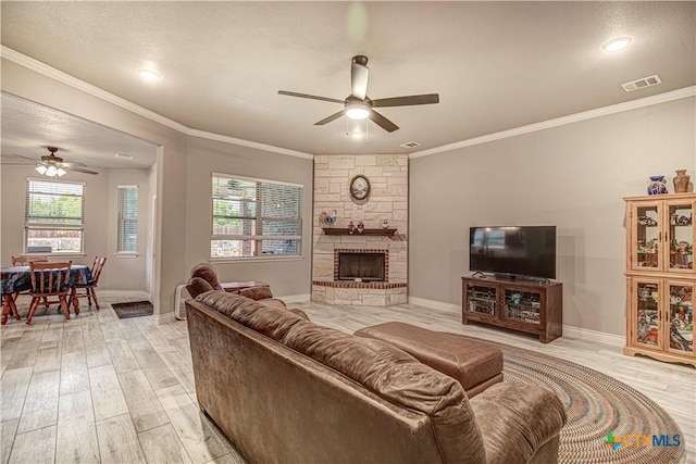 living room with a textured ceiling, ornamental molding, ceiling fan, a fireplace, and light hardwood / wood-style floors