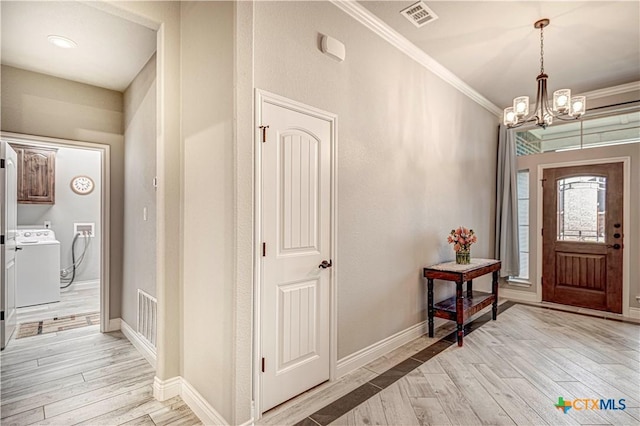 foyer entrance with ornamental molding, washer and dryer, a chandelier, and light wood-type flooring