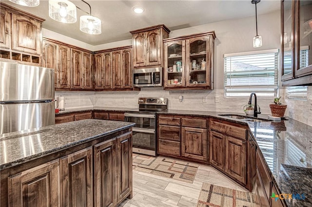 kitchen featuring pendant lighting, sink, backsplash, stainless steel appliances, and dark stone counters